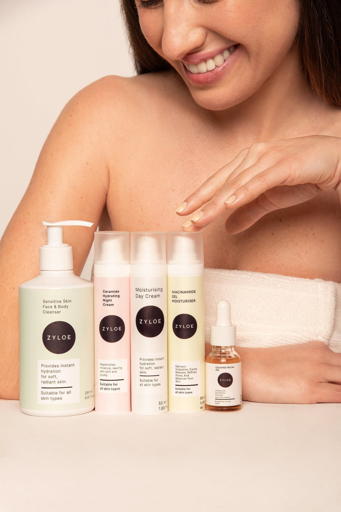 Woman with Zyloe skincare products (cleanser, day cream, moisturizer, serum) displayed in front of her.
