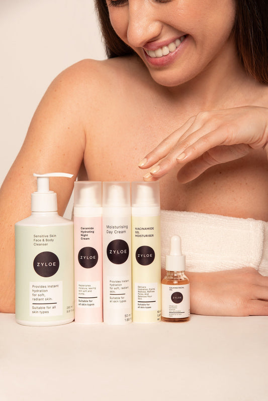 Woman with Zyloe skincare products (cleanser, day cream, moisturizer, serum) displayed in front of her.
